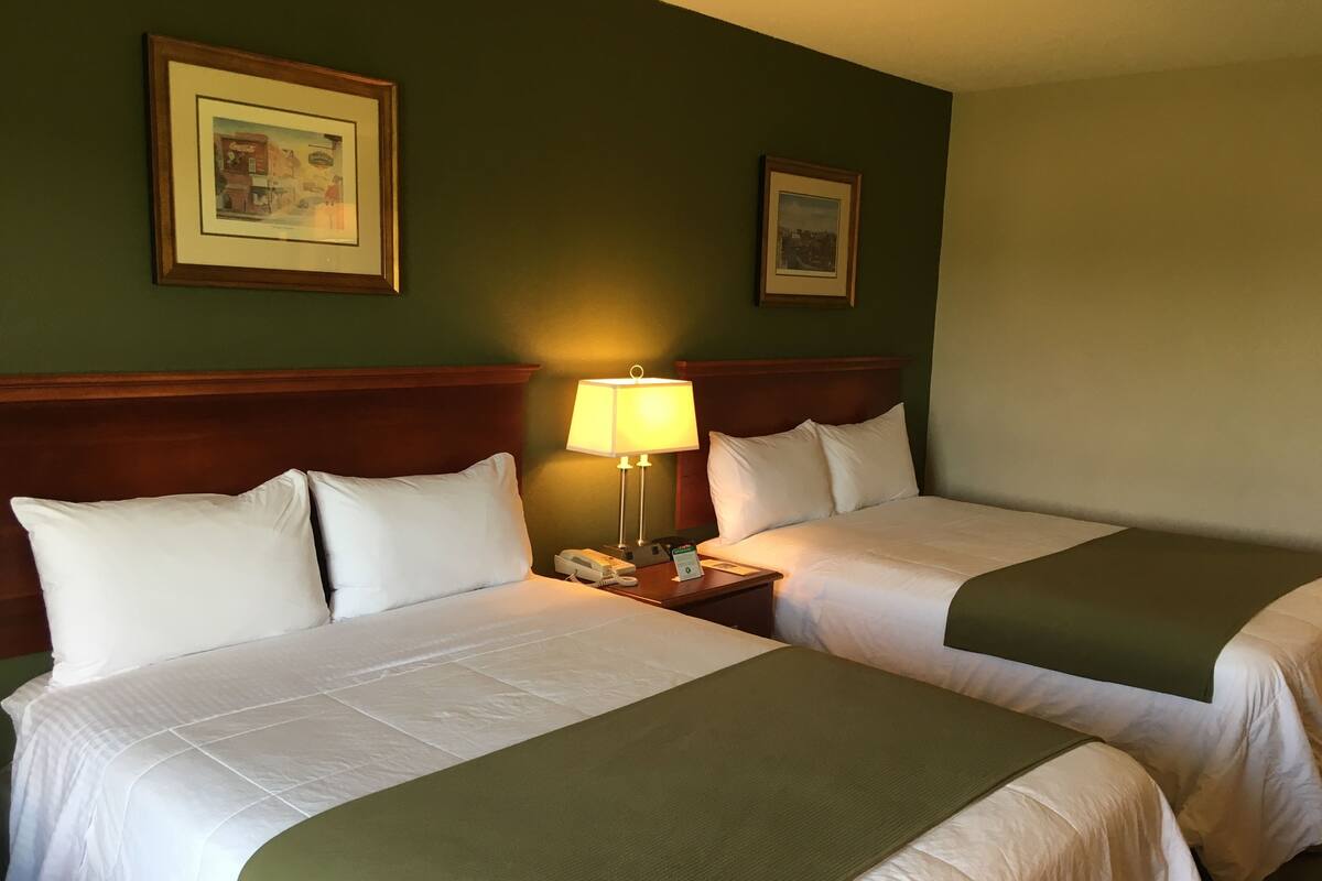 A hotel room with two beds, a nightstand with a lamp, and two framed pictures on the wall.