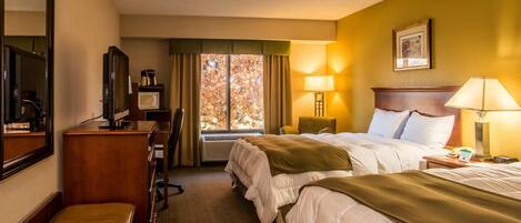 A hotel room with two beds, a desk with a computer, a television, and a window with curtains.