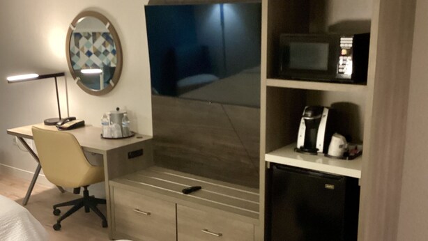 A hotel room with a bed, a desk with a chair, a minibar, a television, and a mirror. - Holiday Inn Express Hotels & Suites Cocoa Beach by IHG (Cocoa Beach)
