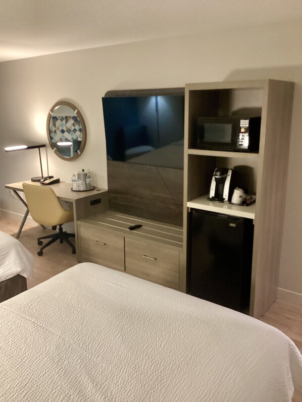 A hotel room with a bed, a desk with a chair, a minibar, a television, and a mirror. - Holiday Inn Express Hotels & Suites Cocoa Beach by IHG (Cocoa Beach)