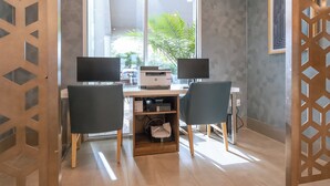 A modern office space with two desks, each with a computer and a printer. There are two chairs, a bookshelf, and a window with a view of greenery outside. - Holiday Inn Express Hotels & Suites Cocoa Beach by IHG (Cocoa Beach)