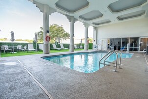 Un área de piscina interior con vista despejada, sillas de descanso y una zona de estar cubierta.