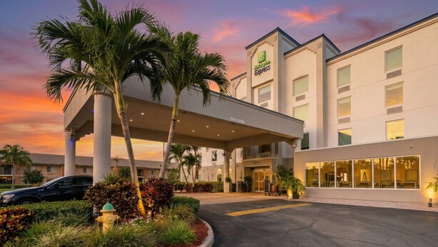 A hotel with a covered entrance, palm trees, and a sunset sky.