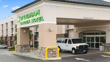 Entrada del Hotel Wyndham Garden con una camioneta blanca estacionada frente a ella, cielo despejado y un letrero que indica una altura libre de 14 pies.