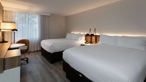 A hotel room with two beds, a desk, a chair, and a lamp.