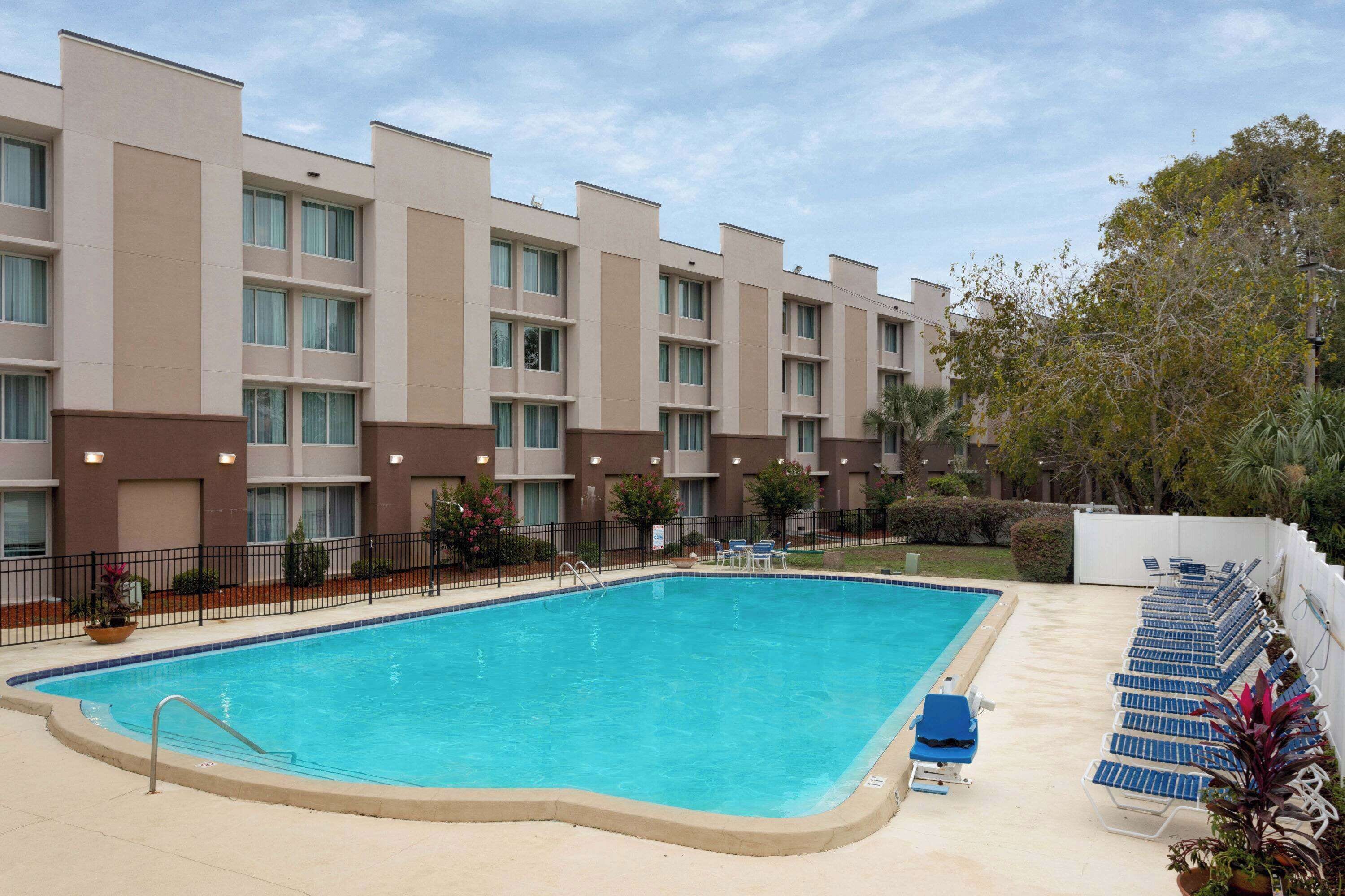 Une piscine avec des chaises longues et, au fond, un bâtiment doté de nombreux balcons.