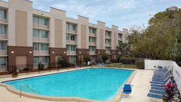 Une piscine avec des chaises longues et, au fond, un bâtiment doté de nombreux balcons.