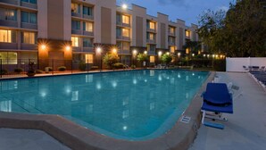 A hotel with a swimming pool, lounge chairs, and a well-lit exterior.