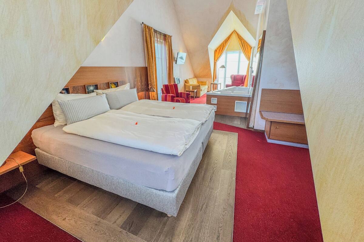A hotel room with a large bed, a desk, a chair, and a red carpet.