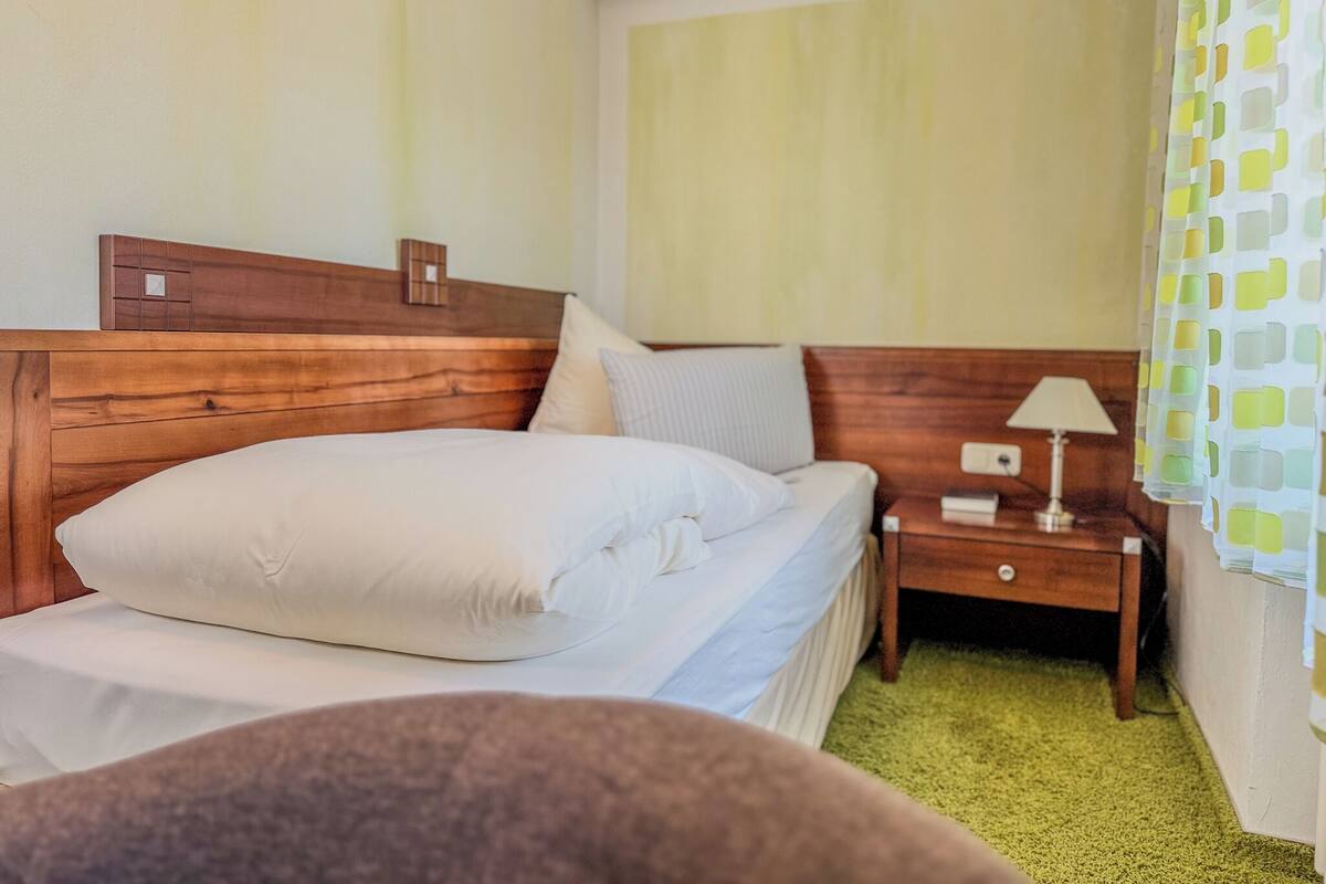 A hotel room with a wooden headboard, a bed with white linens, a nightstand with a lamp, and a green carpet.