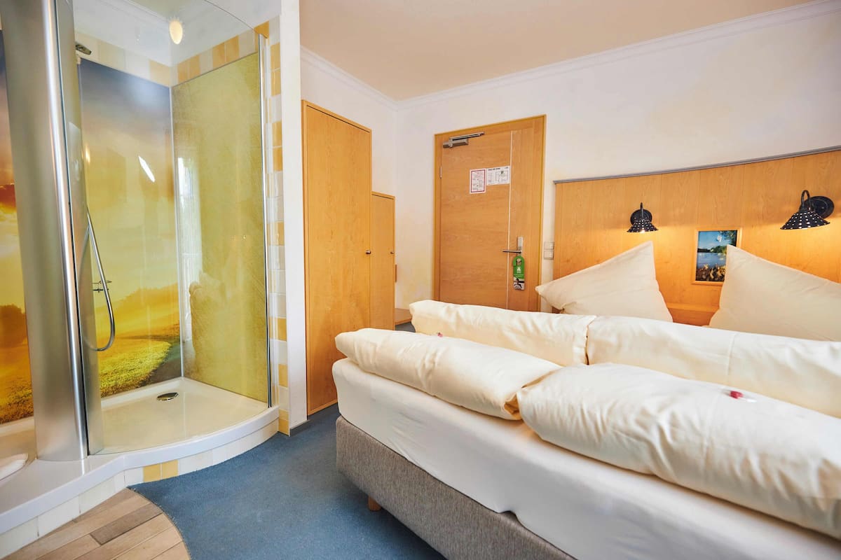 A hotel room with a glass-enclosed shower, a bed with white linens, and a wooden headboard.