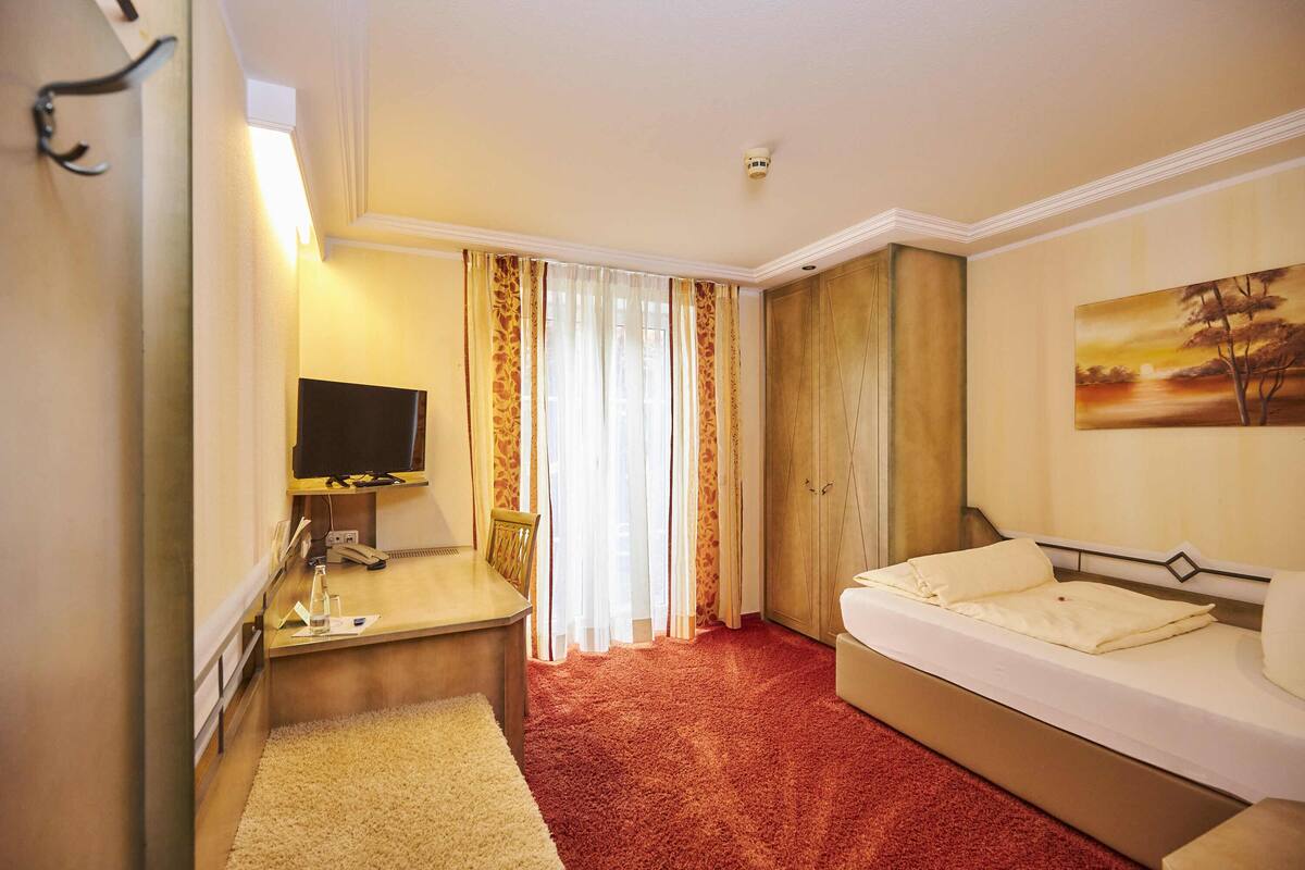 A hotel room with a bed, a desk with a computer, a TV, and a painting on the wall.