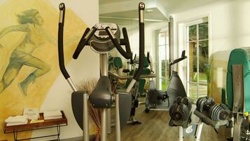 Un gimnasio con equipamiento de ejercicio, un mural y una ventana con vistas a zonas verdes.