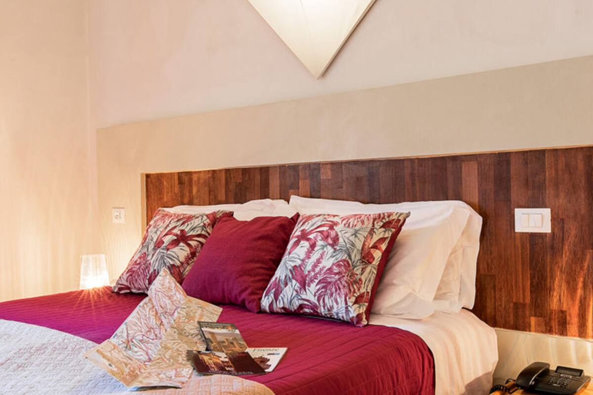A hotel room with a wooden headboard, a red bedspread, and a single bedside table with a phone.