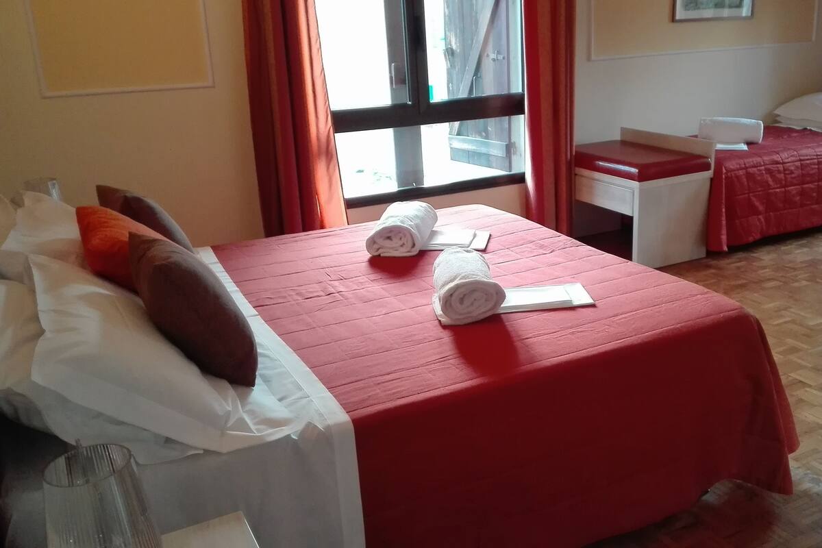 A hotel room with a bed, a small desk, and a chair. There are towels on the bed and a window with curtains.