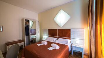 A hotel room with a bed, a desk, a chair, a wardrobe, and a nightstand.