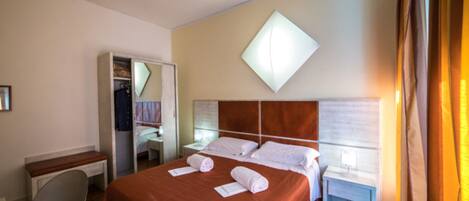Una habitación de hotel con una cama, un escritorio, una silla, un armario y una mesita de noche.