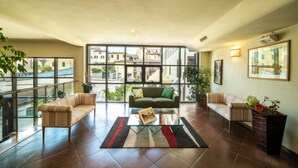 A spacious living area with a sofa, a coffee table, and a view of buildings through large windows. - Hotel La Vecchia Cartiera (Colle di Val d'Elsa)