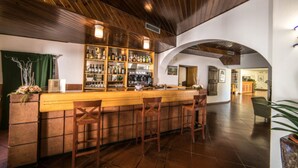 A bar area with wooden bar stools, a counter with bottles, and a tiled floor. - Hotel La Vecchia Cartiera (Colle di Val d'Elsa)