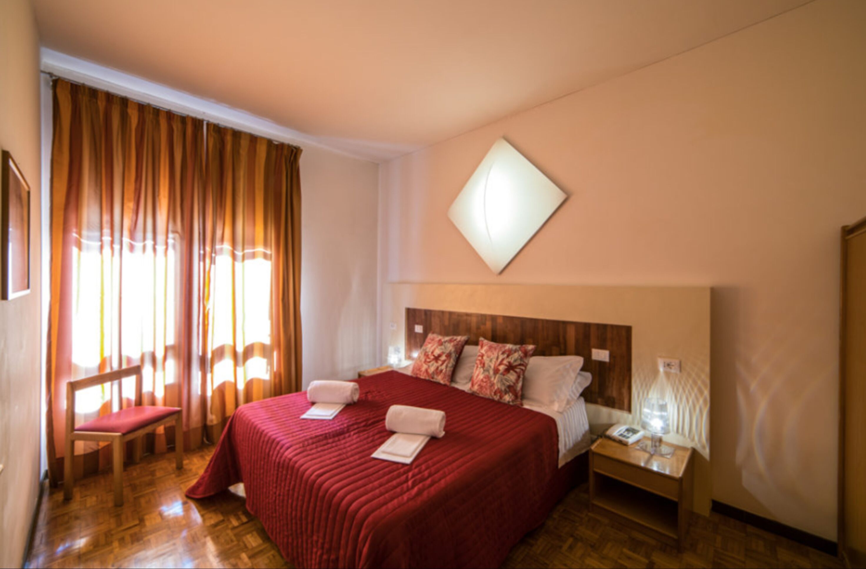 Habitación de hotel con una cama grande, cabecera de madera, mesita de noche y una silla.
