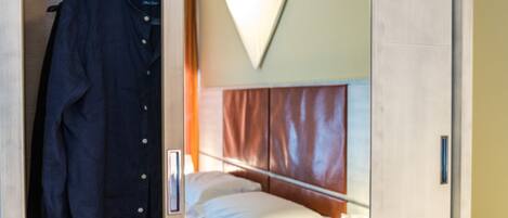 Habitación de hotel con cama, armario colgante y lámpara fijada a la pared.