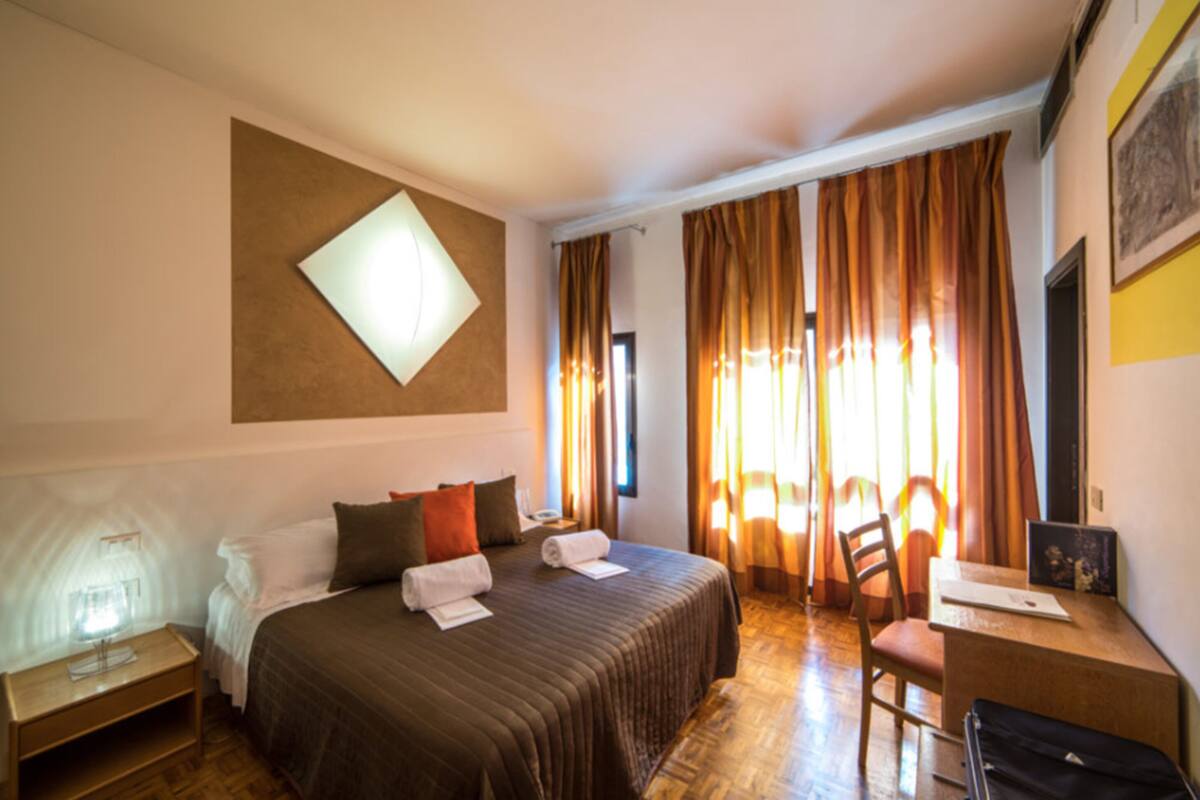 A hotel room with a bed, a desk, a chair, and a window with curtains.