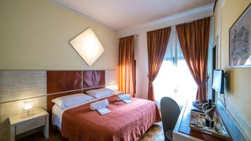 Una camera d'albergo con un letto, un comodino, una sedia e una scrivania con un vassoio.