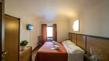 A hotel room with a bed, a bedside table, a TV, and a window with curtains.