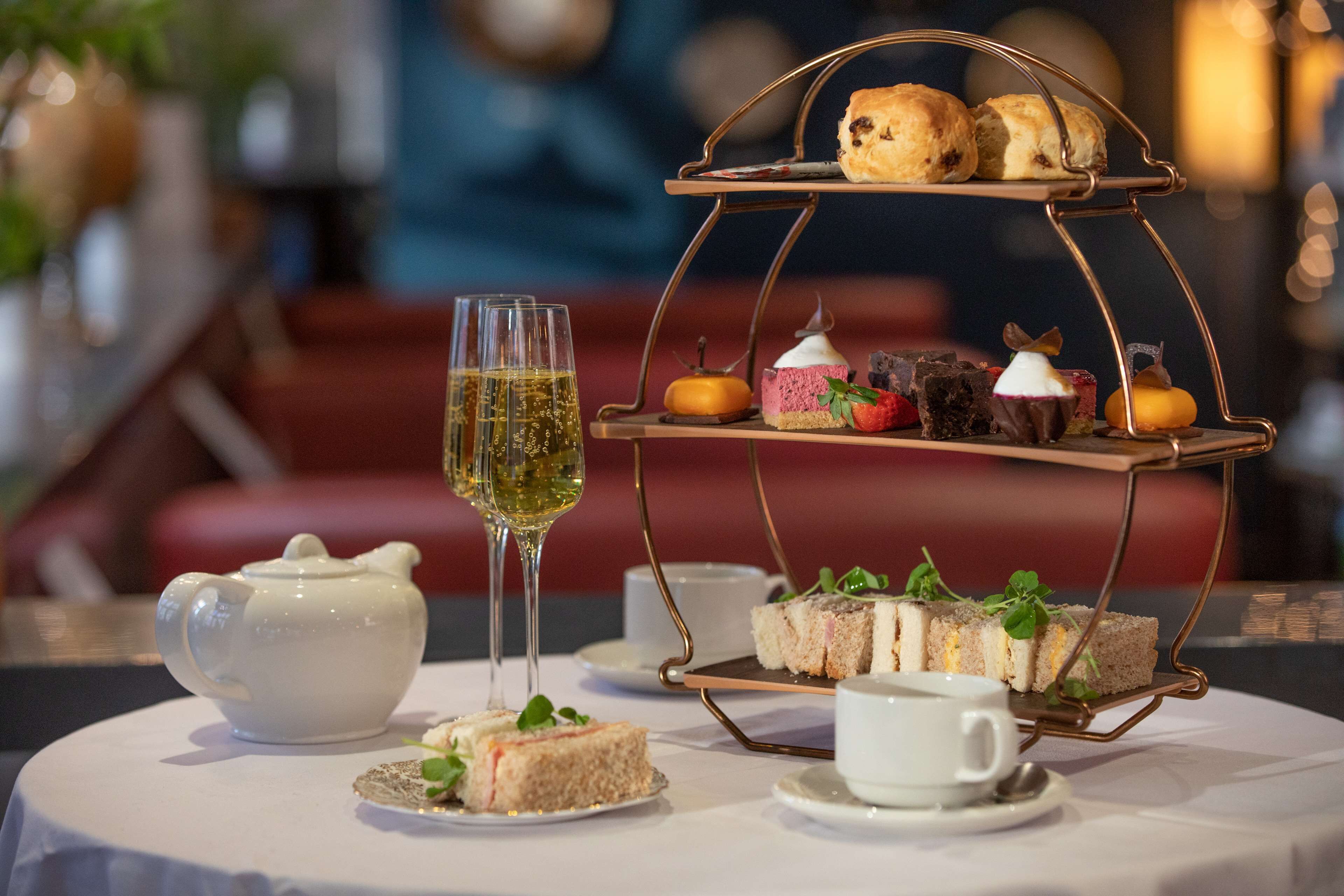 A table with a tea set, a glass of wine, and a tiered dessert stand with various pastries and sandwiches.