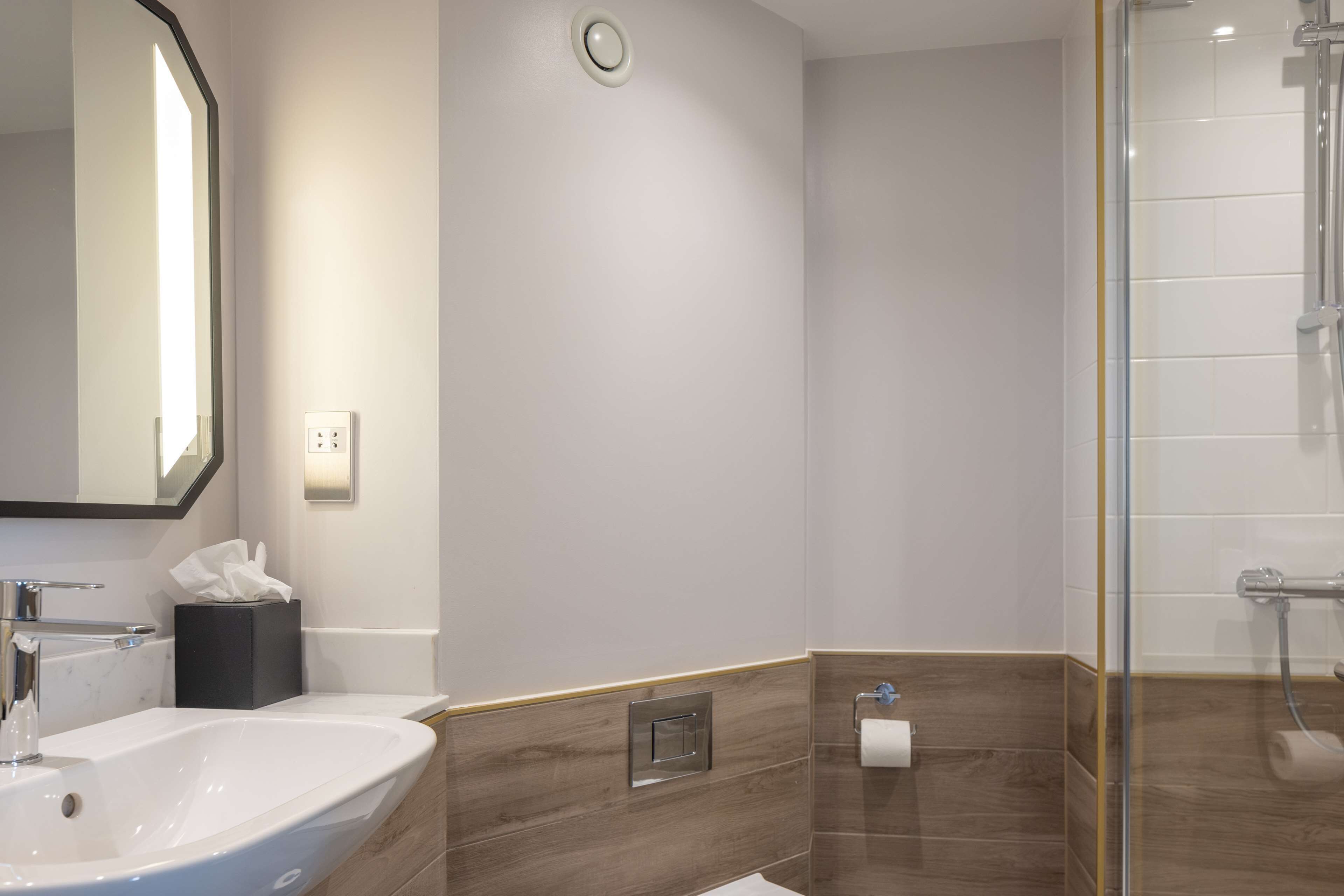 Une salle de bain moderne avec un grand miroir, un lavabo, un distributeur de serviettes et un espace douche.