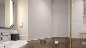 Une salle de bain moderne avec un grand miroir, un lavabo, un distributeur de serviettes et un espace douche.