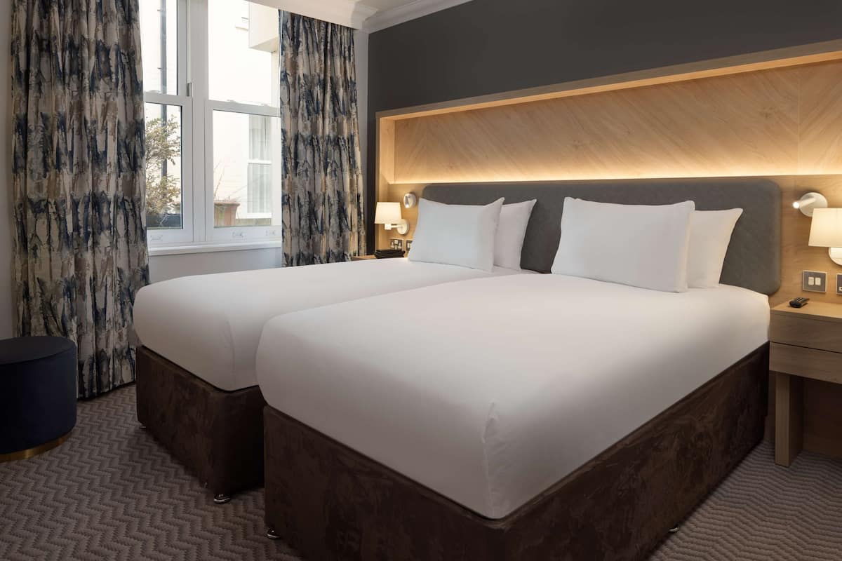 A double bed with a wooden headboard, two bedside tables, a nightstand, and a window with curtains.