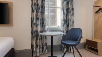 A hotel room with a bed, a round table with a sink, a blue chair, and a wooden cabinet.