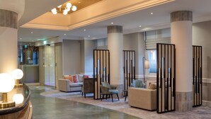 Un vestíbulo amplio con diseño moderno, que incluye una mesa de recepción, zona de estar con sofás y sillones, y columnas decorativas.