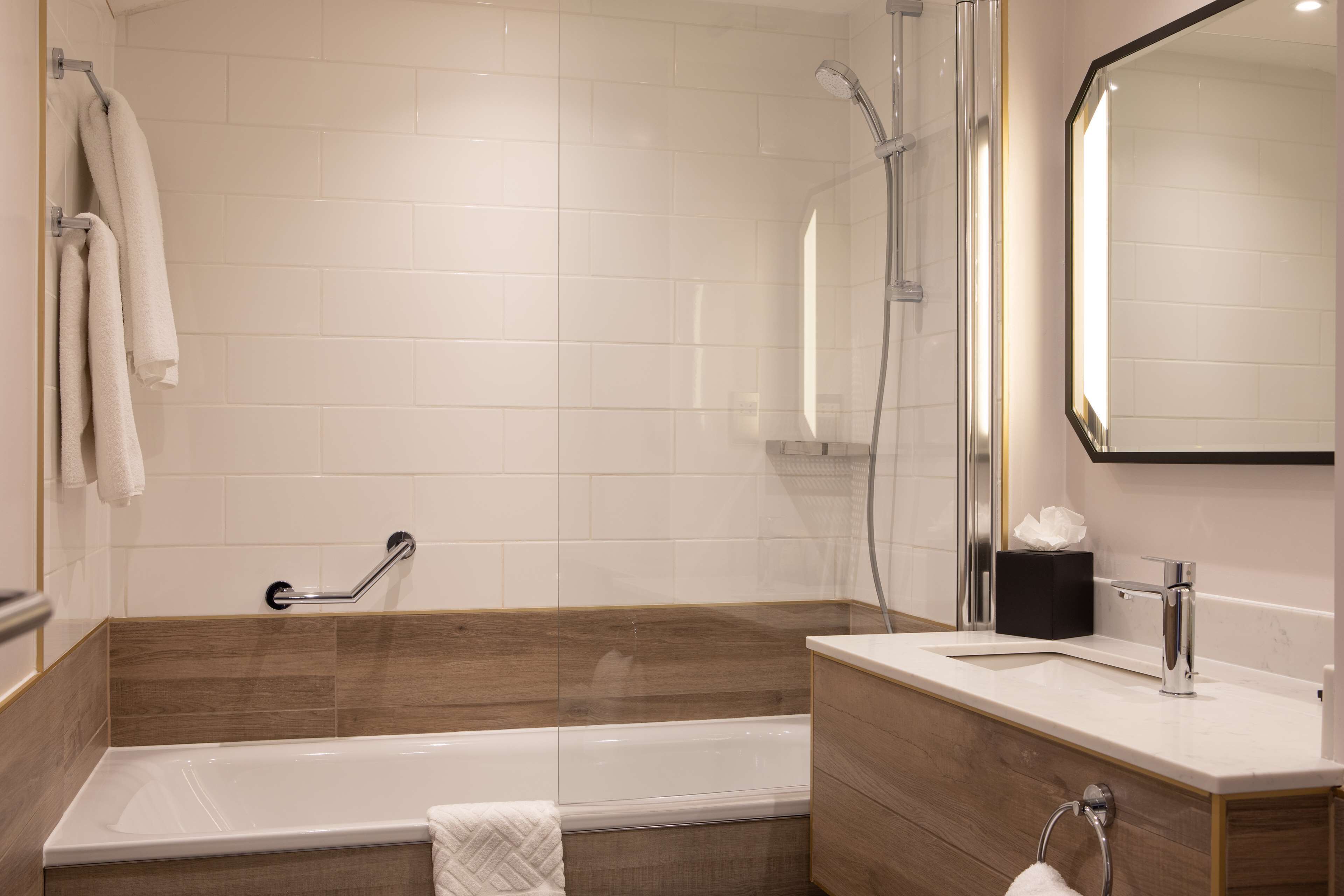A modern bathroom with a bathtub, a shower, a vanity with a mirror, and a towel rack.