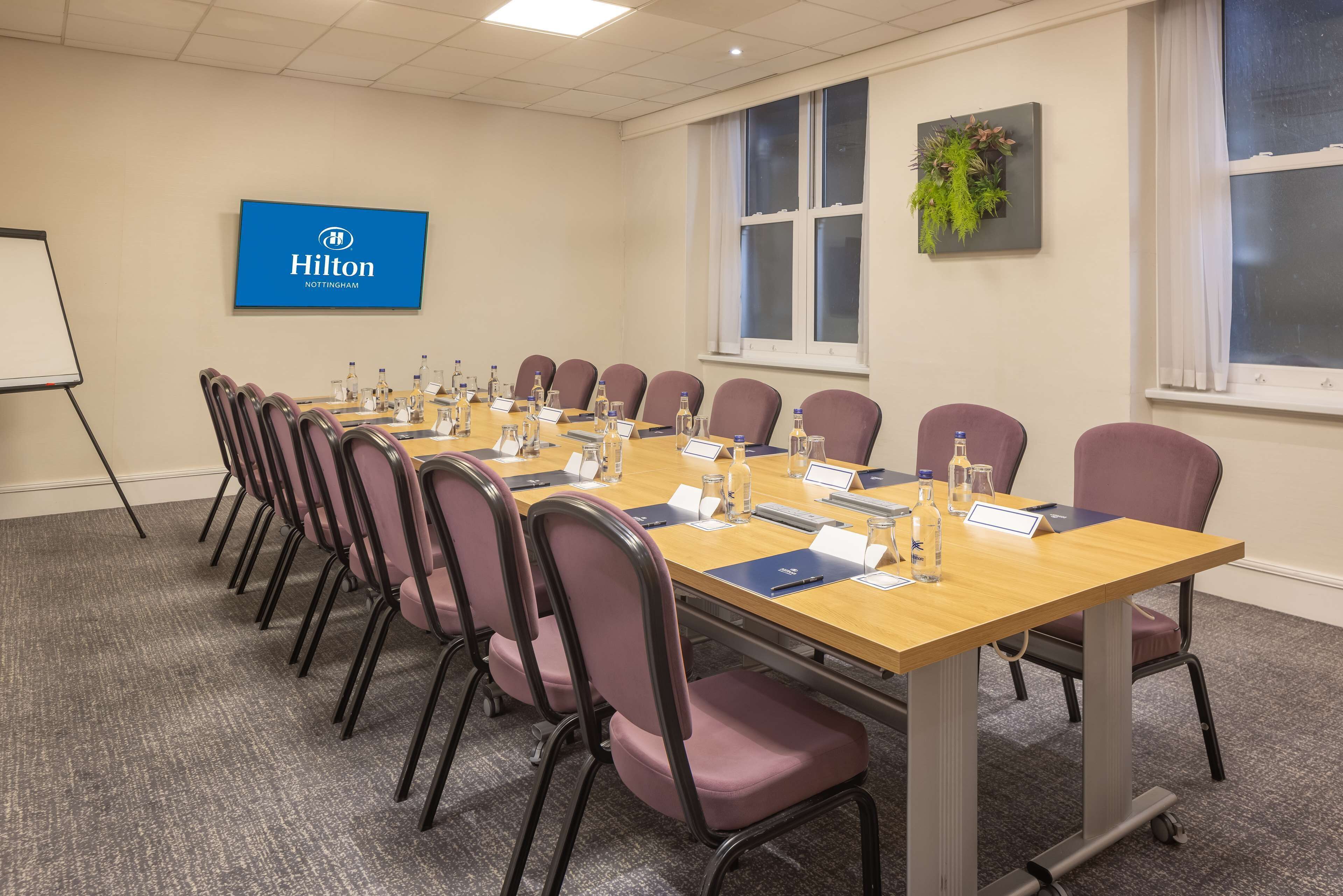 A conference room with a long table, chairs, nameplates, water bottles, and a Hilton Nottingham sign on the wall.