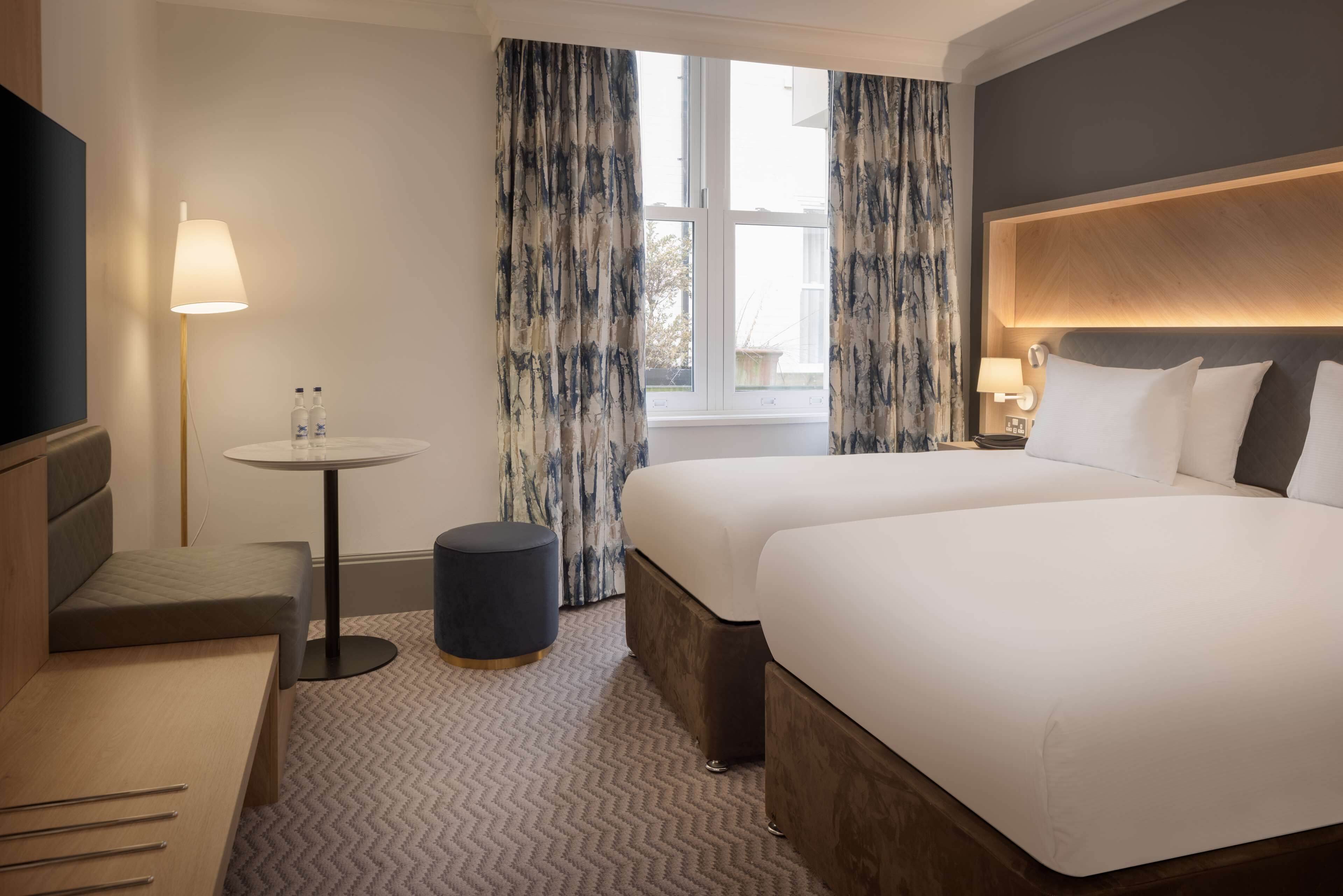 A hotel room with a bed, a desk, a chair, a round table, and a TV.