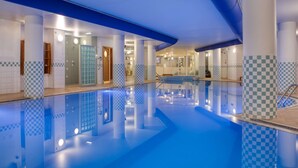 Una amplia piscina interior con suelo de baldosas de cuadros, rodeada de columnas blancas con diseños de cuadros azules y blancos, y una barrera de vidrio.