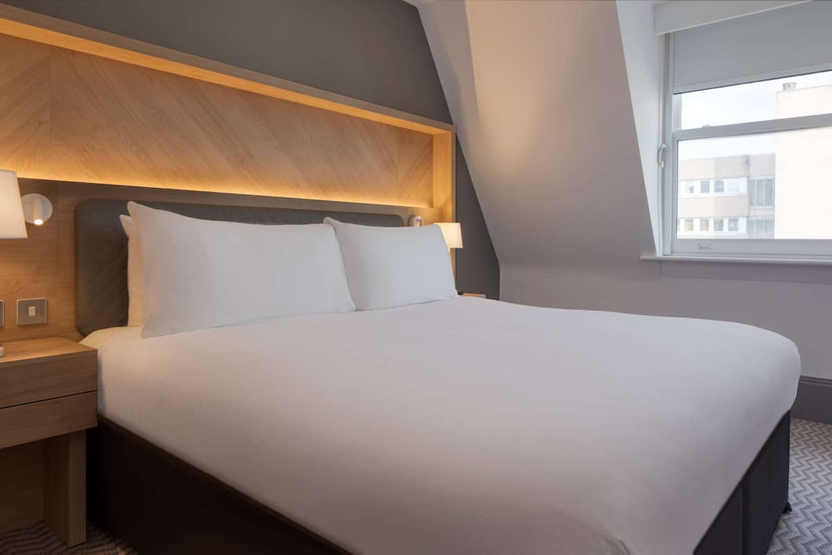 A neatly made bed with white linens, a wooden headboard, and bedside lamps.