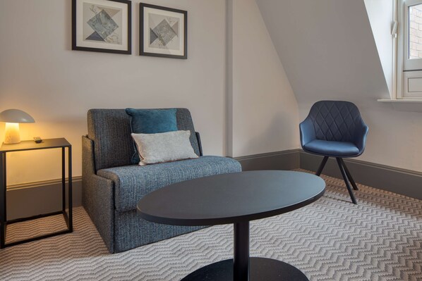 Una sala moderna con un sofá, una mesa redonda, una mesita auxiliar con una lámpara y un sillón azul.