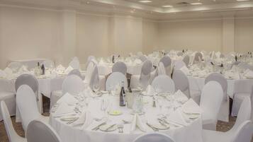 Un salón de banquetes con mesas redondas dispuestas para comer, sillas blancas y una paleta de colores neutros.