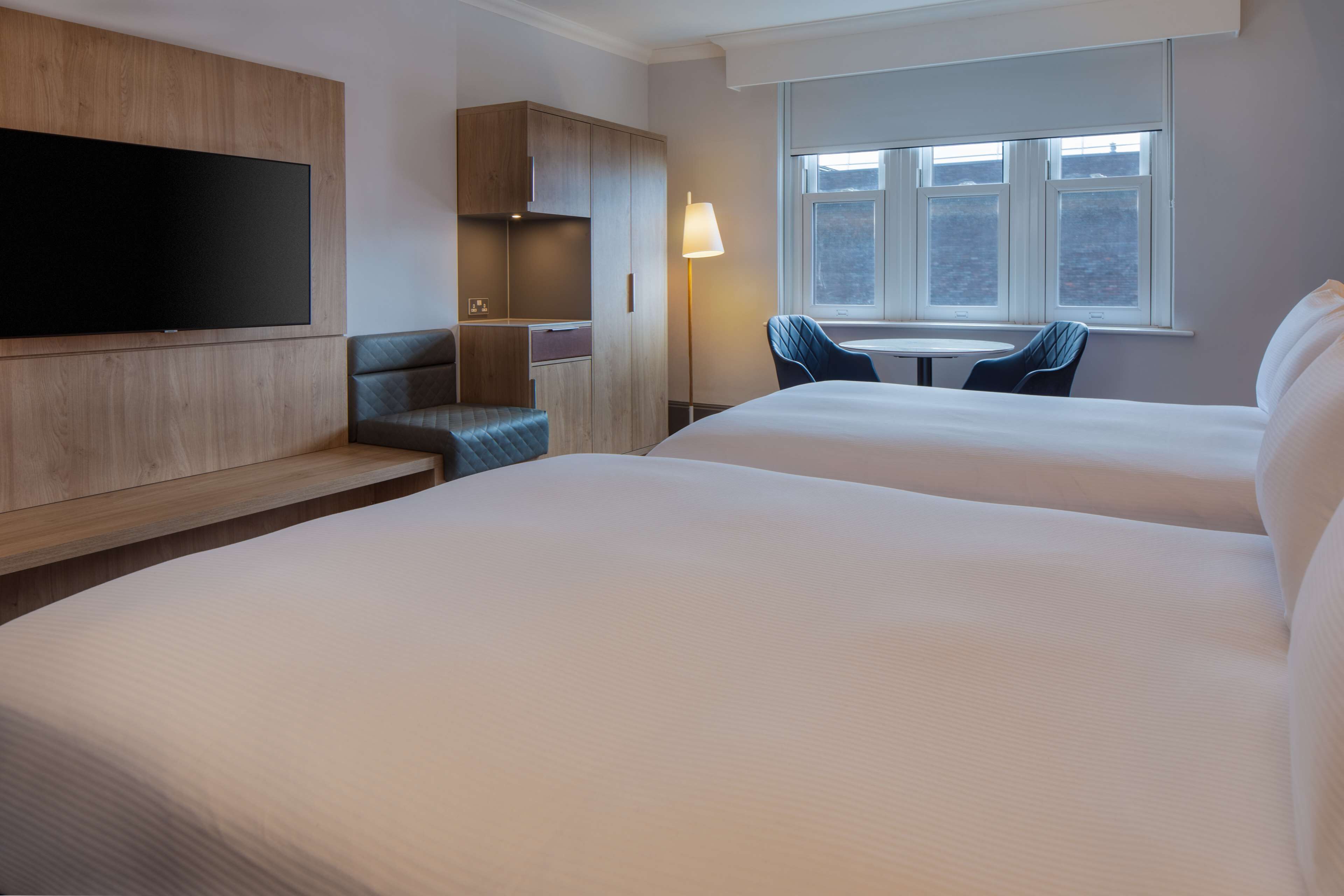Ein Hotelzimmer mit zwei Betten, einem Fernseher, einem Schreibtisch und einem Stuhl.