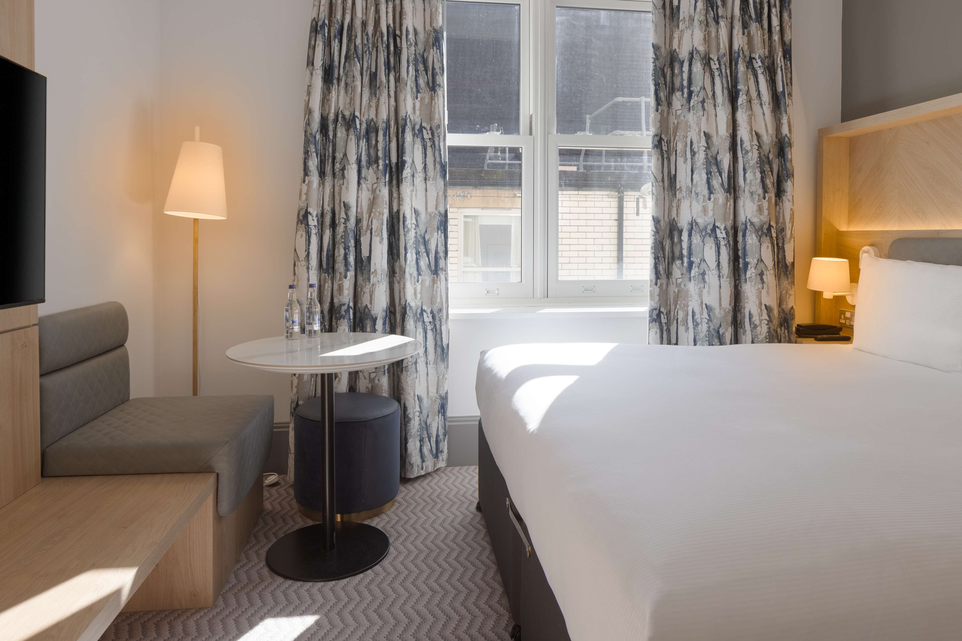 A hotel room with a bed, a desk, a chair, a round table, and a TV.