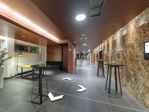 A hotel corridor with directional arrows on the floor, a reception desk, and a seating area. - Hotel Mercure Gdansk Stare Miasto (Gdansk)
