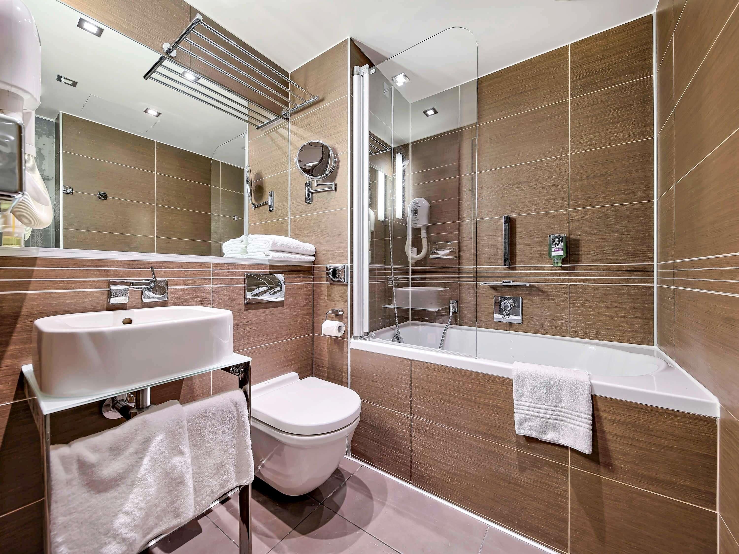 Un bagno moderno con vasca, servizi igienici e lavabo, con rivestimenti in legno e cabina doccia in vetro.