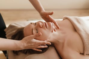 A person lying down with hands placed on their head and neck, suggesting a massage or relaxation session.