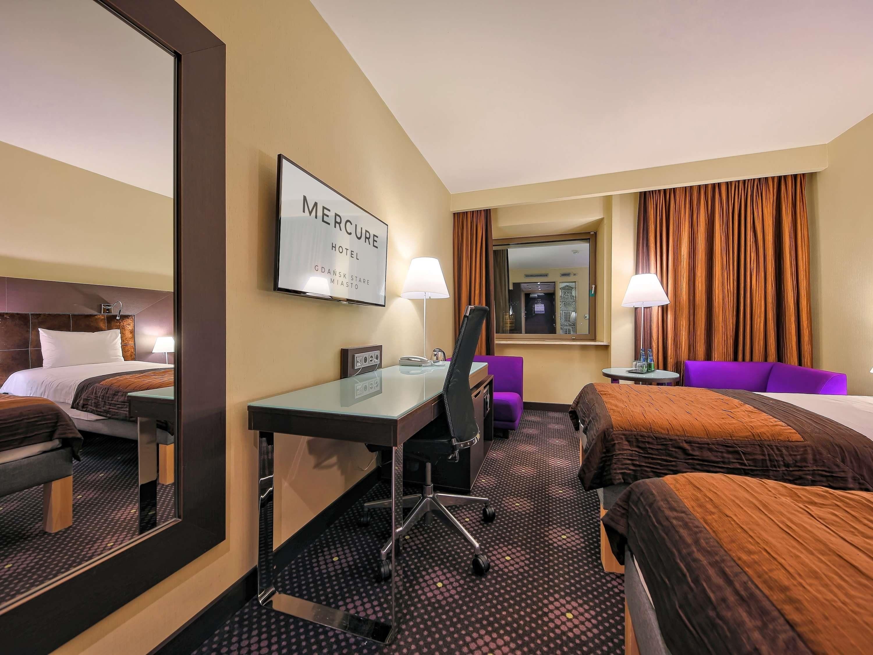 Une chambre d’hôtel avec un lit, un bureau, une chaise et un grand miroir.