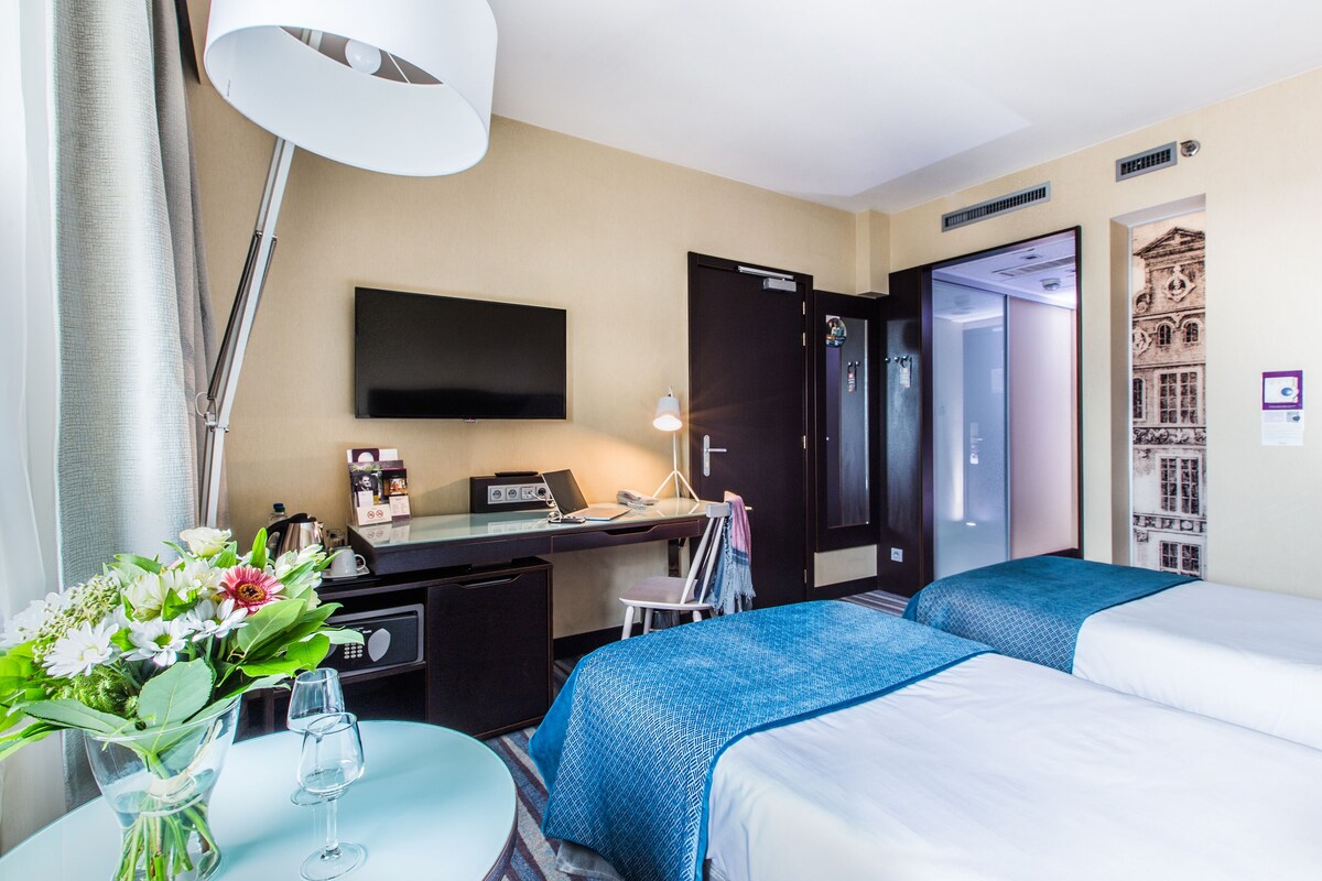A hotel room with two beds, a desk with a computer, a TV, and a desk lamp.