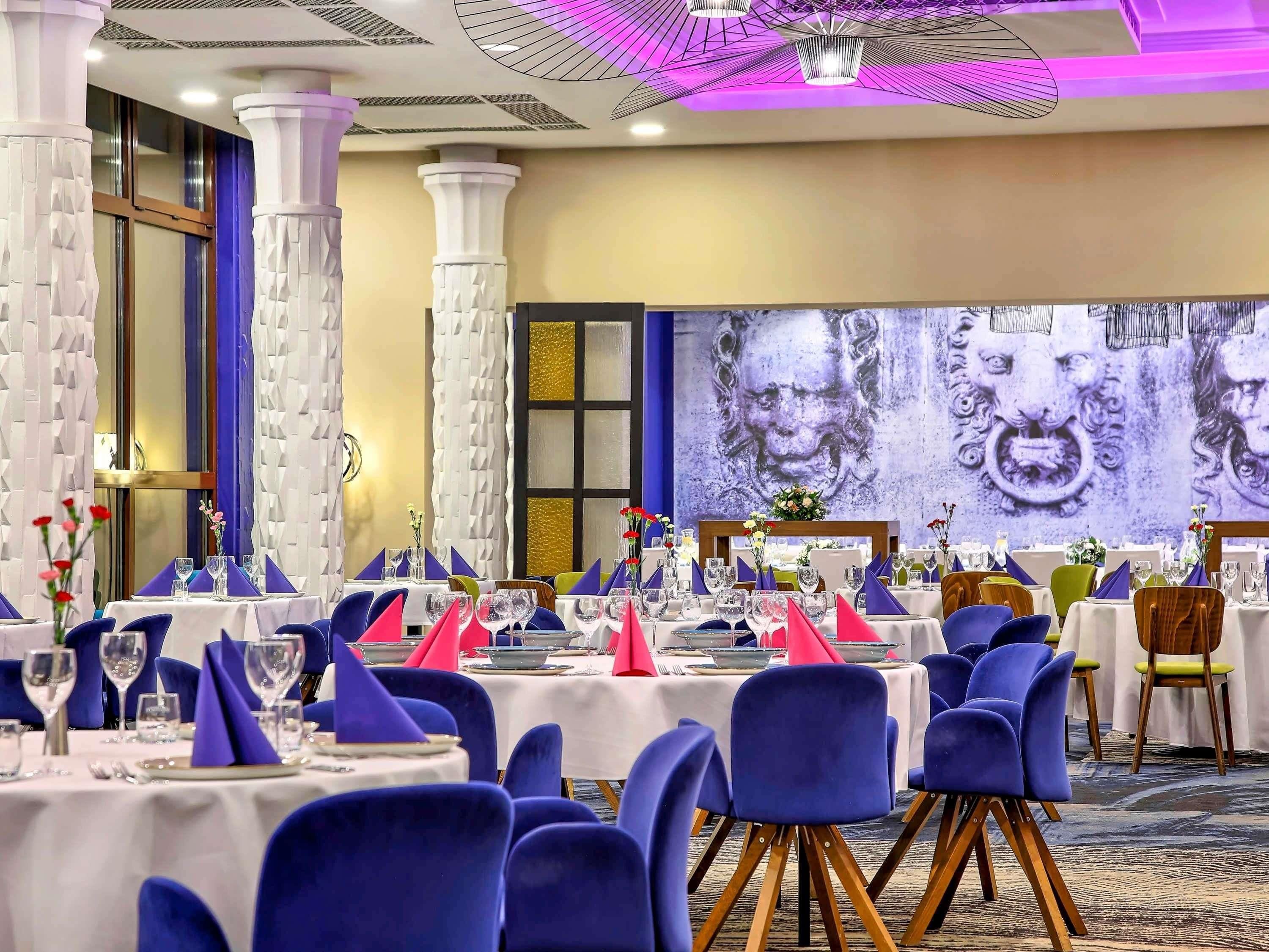 A banquet hall with round tables, blue chairs, and a large mural on the wall.