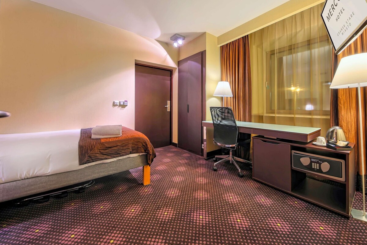 Une chambre d’hôtel équipée d’un lit, d’un bureau, d’une chaise et d’une enseigne indiquant le nom de l’hôtel.
